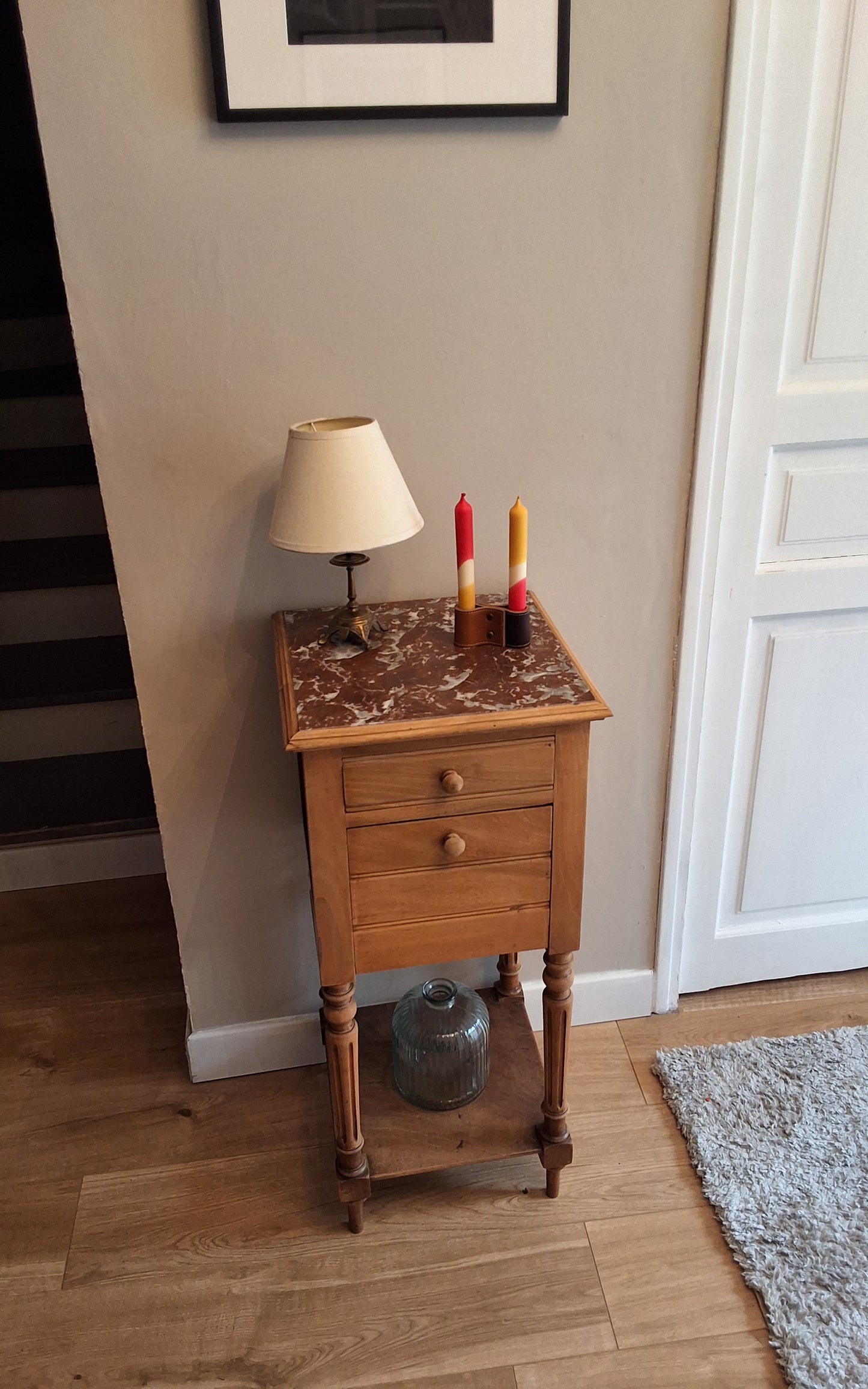Bougeoir pose sur une desserte a plateau de marbre. Petite lampe a cote