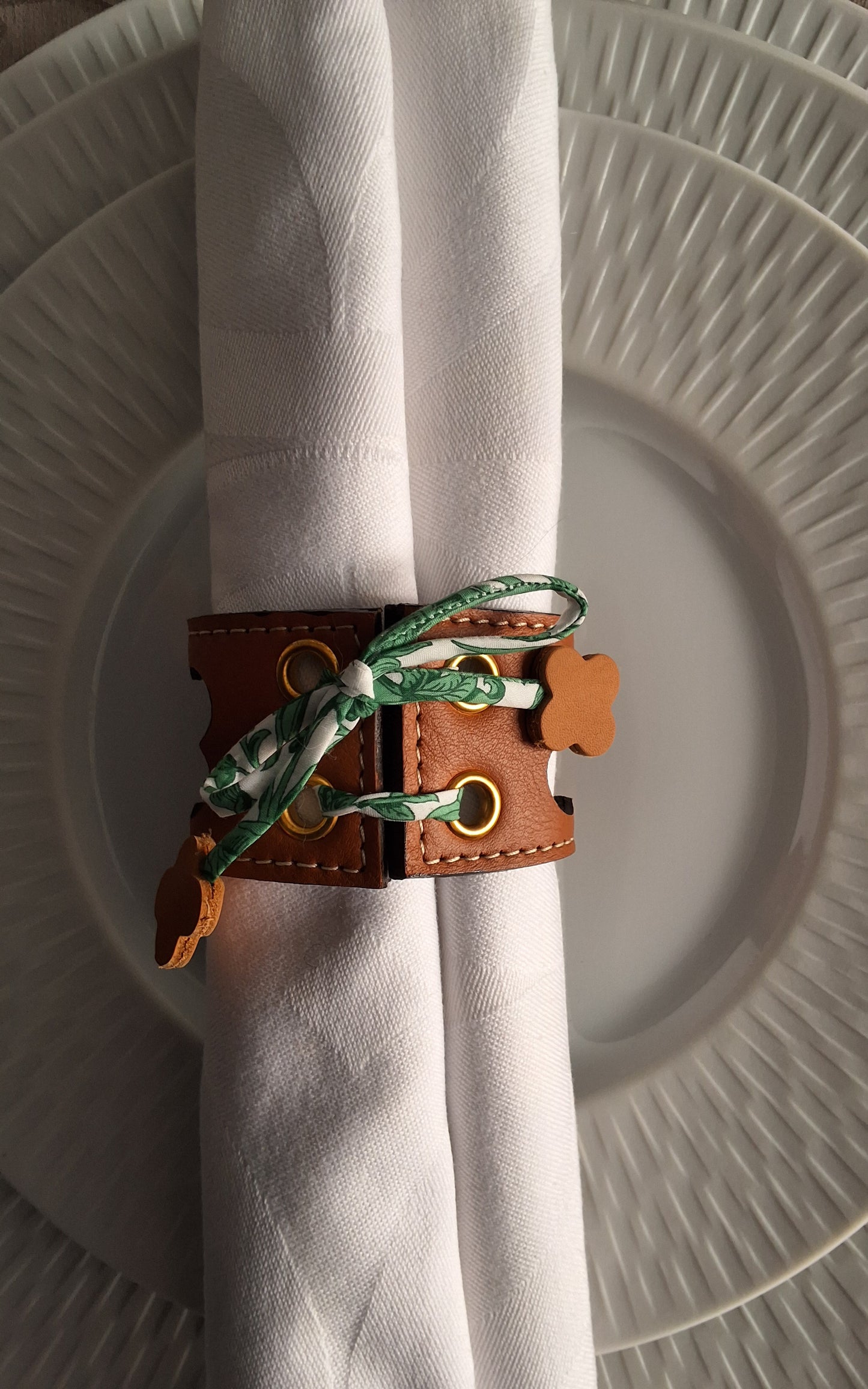 Serviette blanche roulee et tenue par un rond de serviette avec motifs trefle ajouré sur une assiette blanche