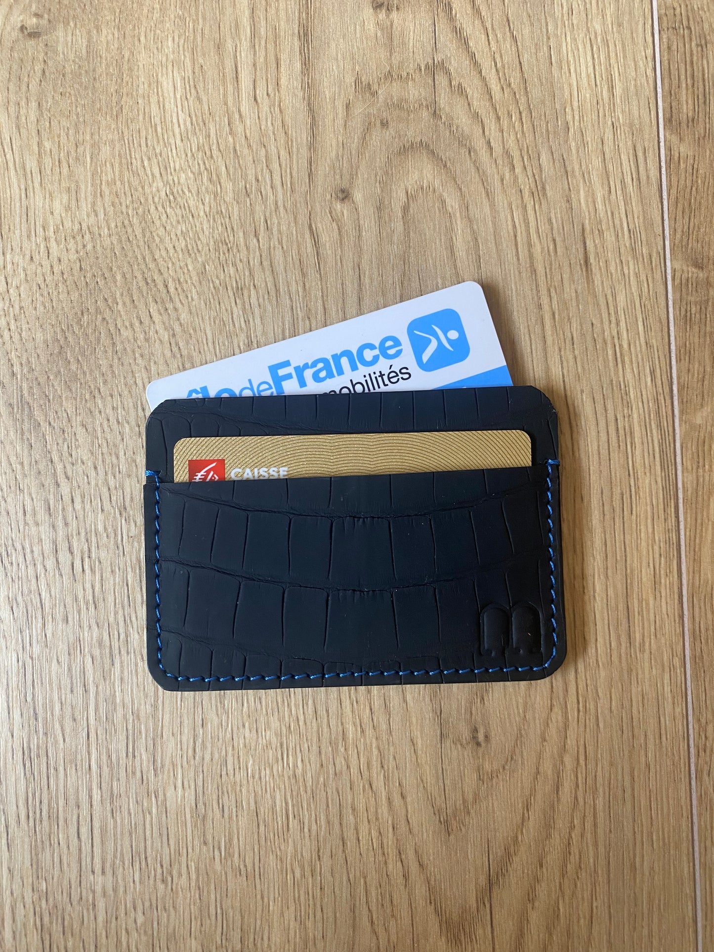 Porte carte en cuir de crocodile noir mat et surpiqure rouge sur le parquet