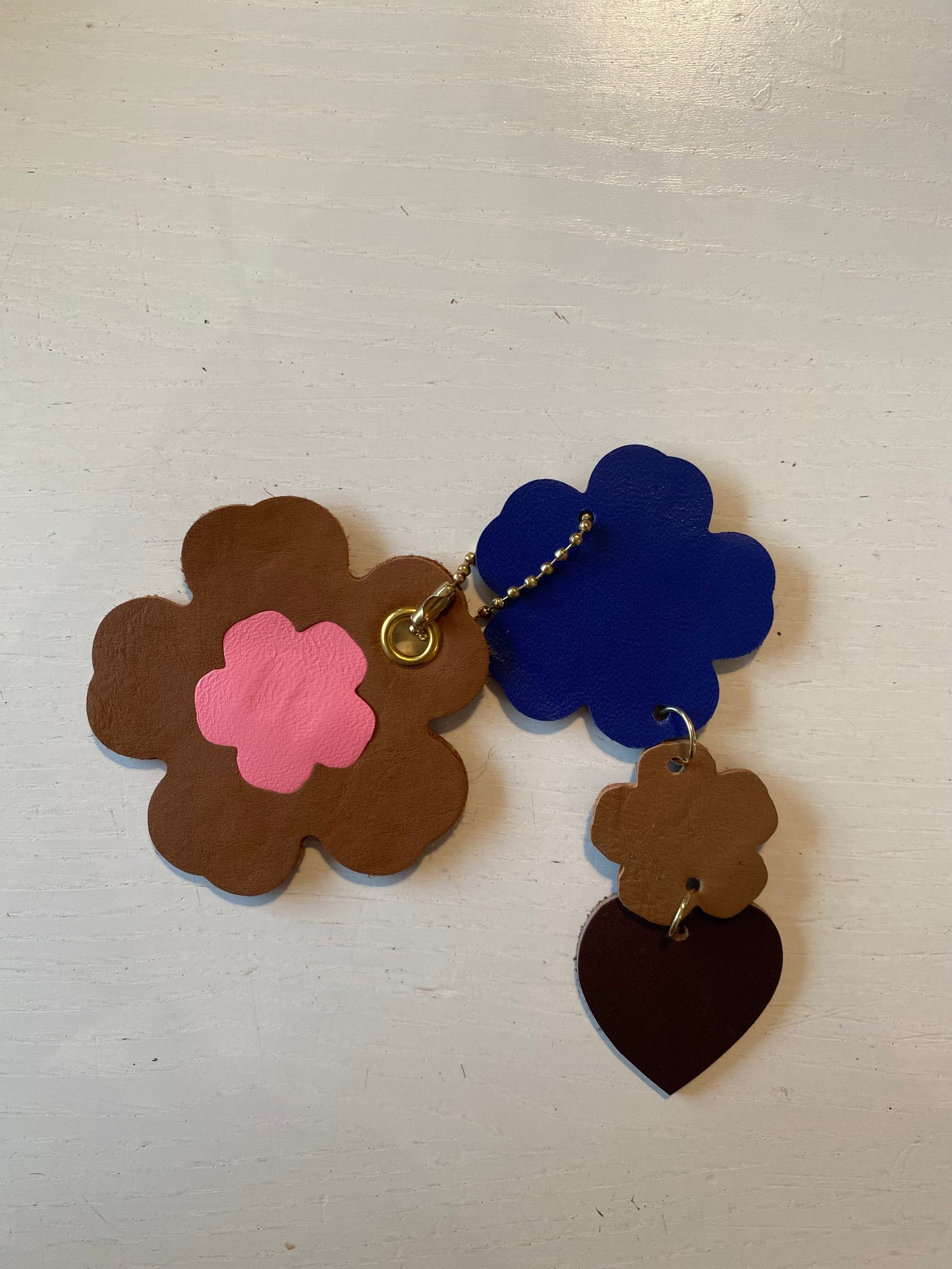 Porte clef en cuir composé de 2 éléments de forme floral et de cœur sur fond blanc