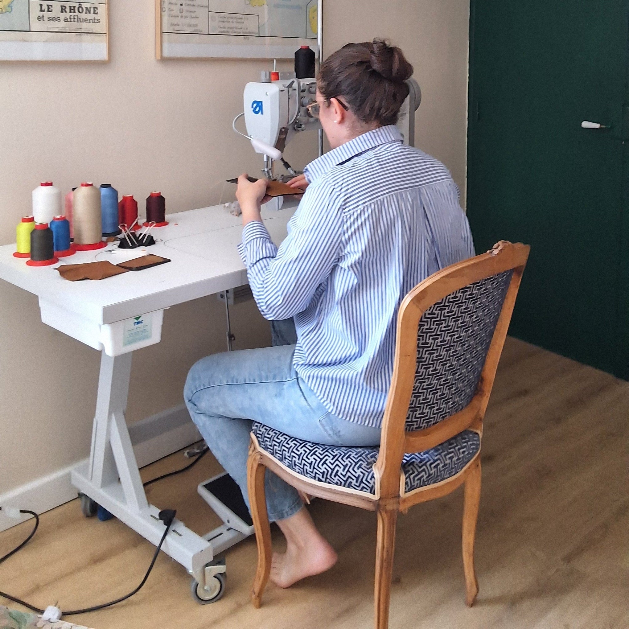 La créatrice entrain de confectionner un porte cartes avec sa machine à coudre dans son atelier.