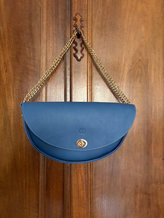 sac demi lune bleu et chainette dorée accroché à la clef d'une armoire en bois.