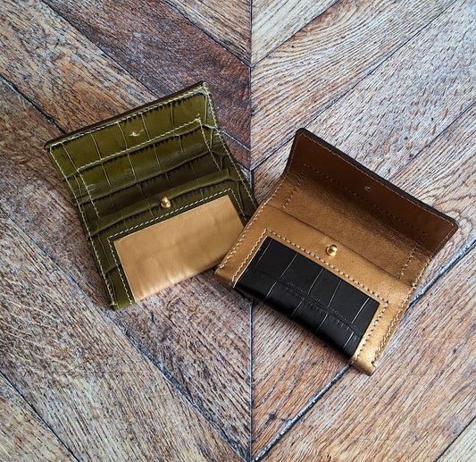 2 portes cartes doré et motif croco vert kaki et noir déplié disposé sur un parquet.