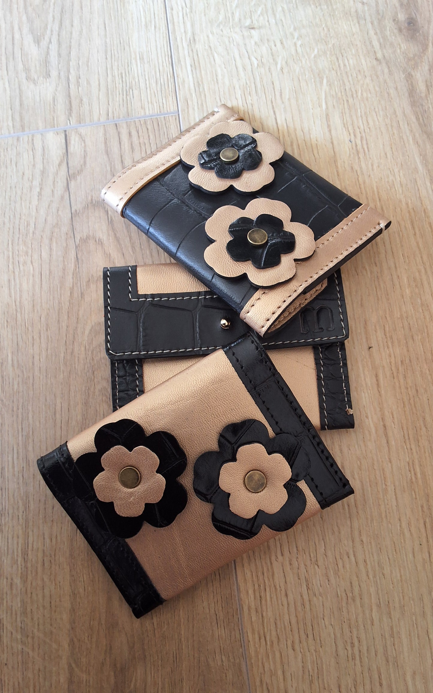 3 porte cartes noir et doré superposés les uns sur les autres verticalement, le premier et le troisième sont de dos et ont deux fleurs cousus.