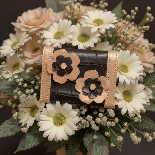 Porte cartes noir et doré avec les fleurs cousus à l'arrière du modèle disposé dans un bouquet de fleurs blanches et roses.