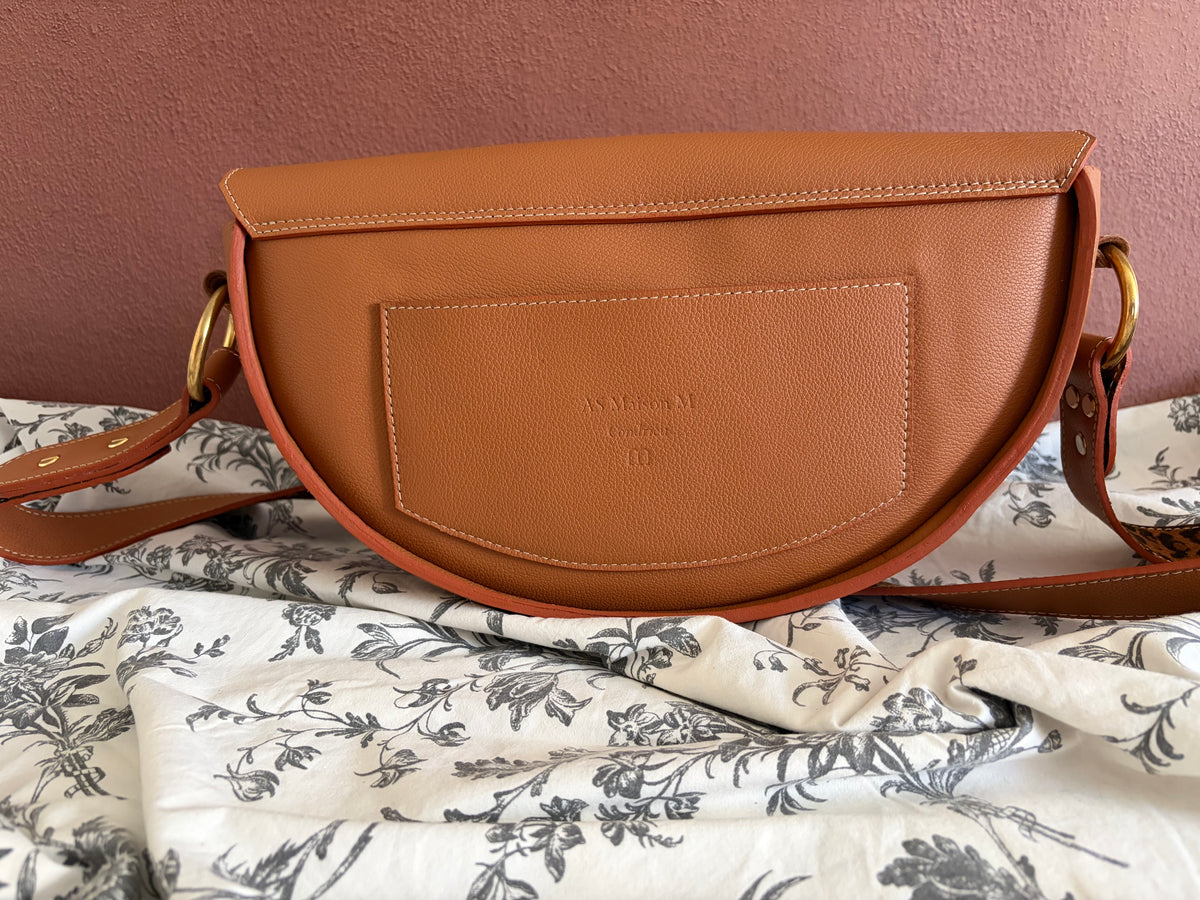 le sac est présenté de dos. il dispose d'une poche plaquée en cuir de la même couleur que le sac. les piqures sont beige