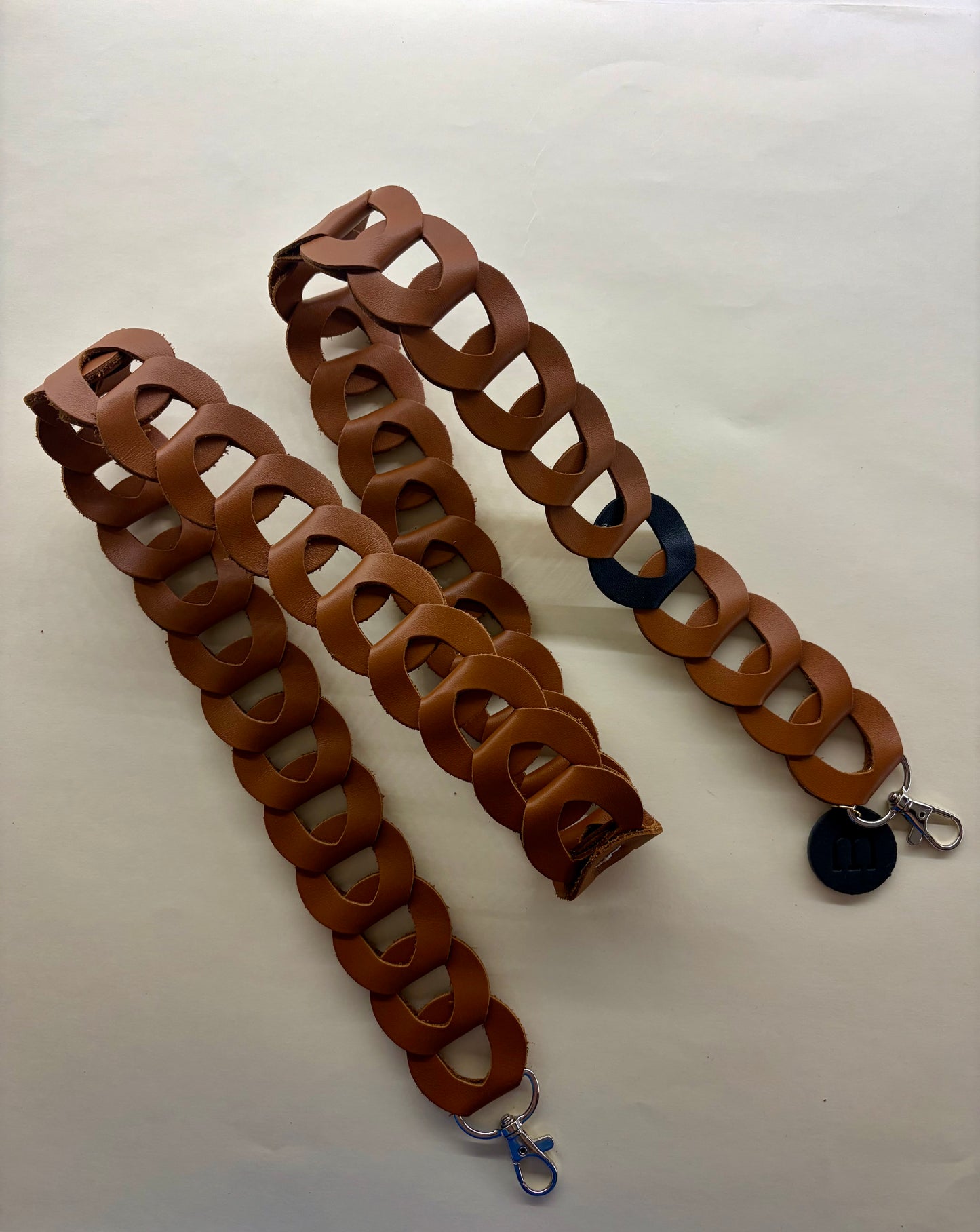 la sangle à portable en maillons de cuir marron est déposé sur un fond blanc