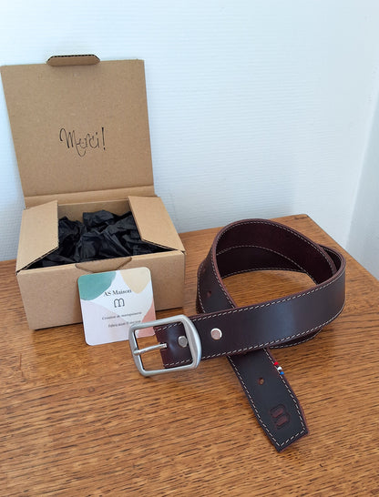 ceinture enroulée et déposée sur un plateau en bois avec le packaging à côté