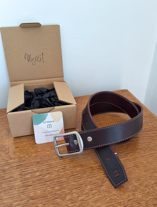 ceinture enroulée et déposée sur un plateau en bois avec le packaging à côté
