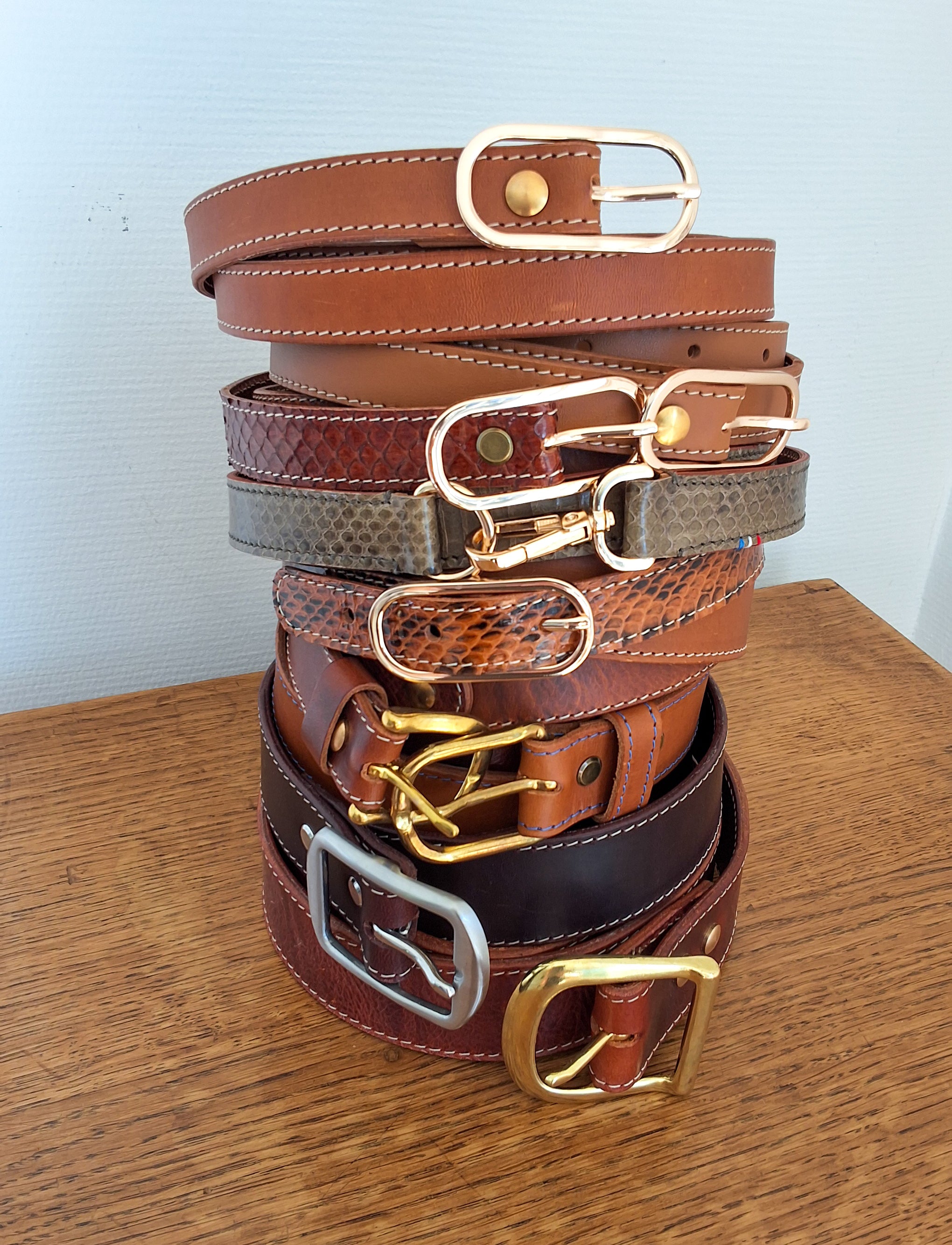 Multitude de ceinture empilées posees sur un meuble en bois 