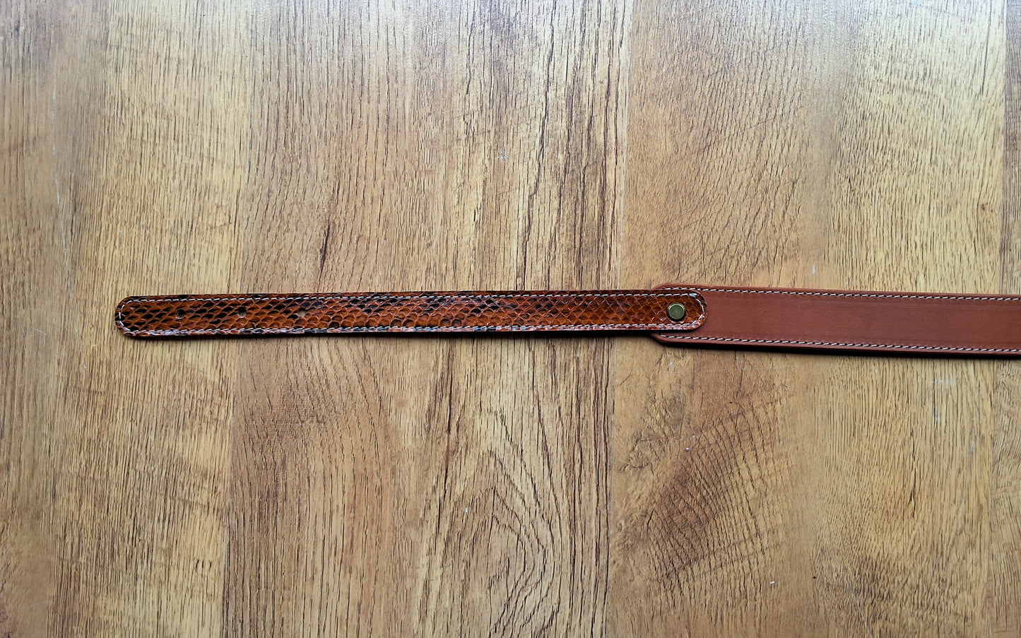 Ceinture en cuir et peau de serpent marron déposée sur un meuble en bois 