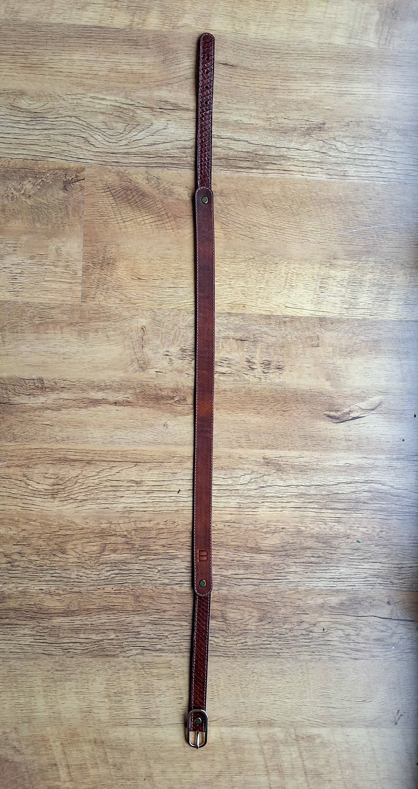 Ceinture en cuir et peau de serpent marron déposée sur un meuble en bois 