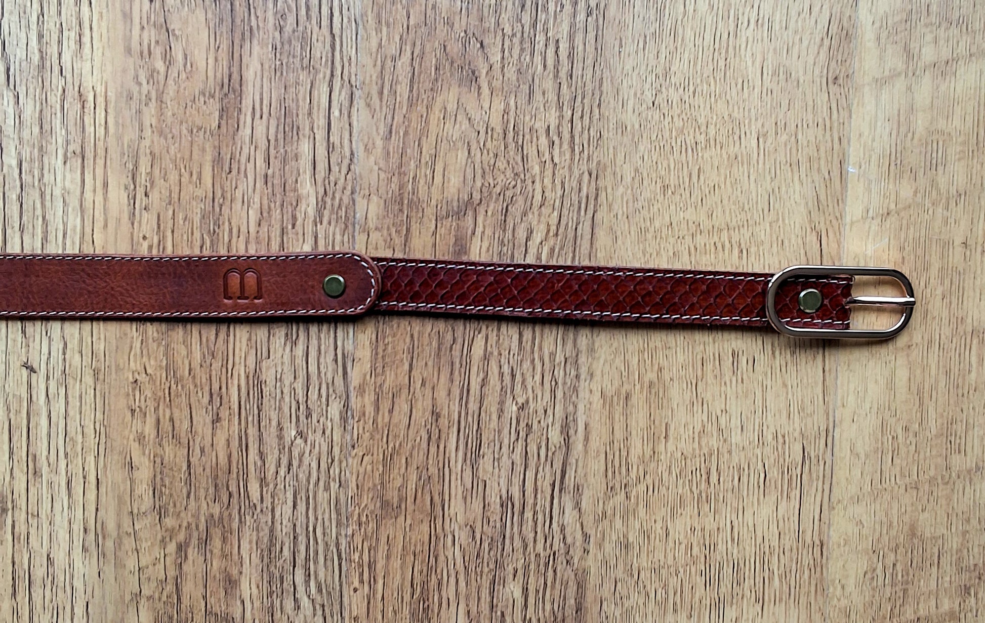 Ceinture en cuir et peau de serpent marron déposée sur un meuble en bois 