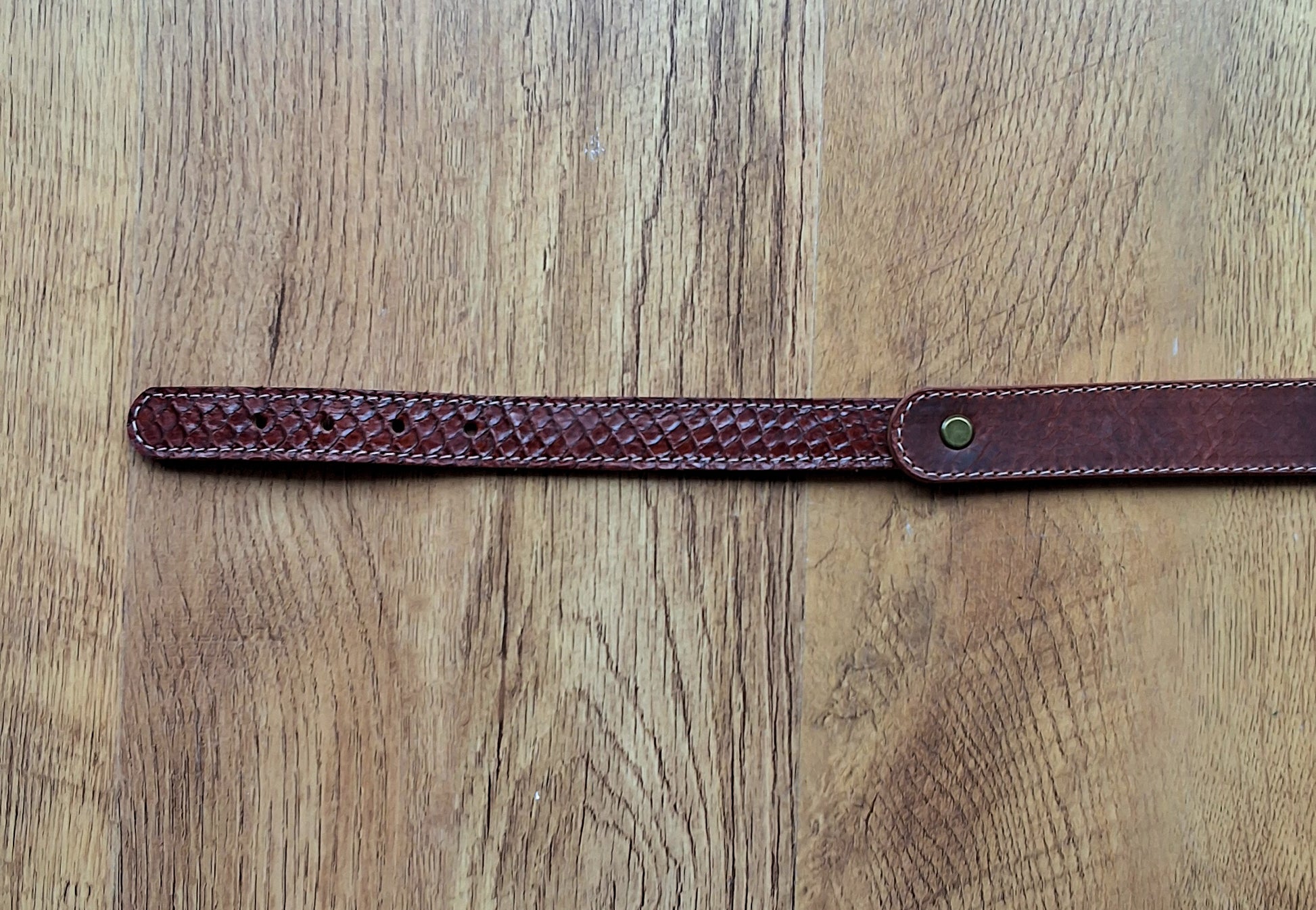 Ceinture en cuir et peau de serpent marron déposée sur un meuble en bois 