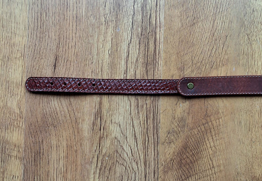 Ceinture en cuir et peau de serpent marron déposée sur un meuble en bois 