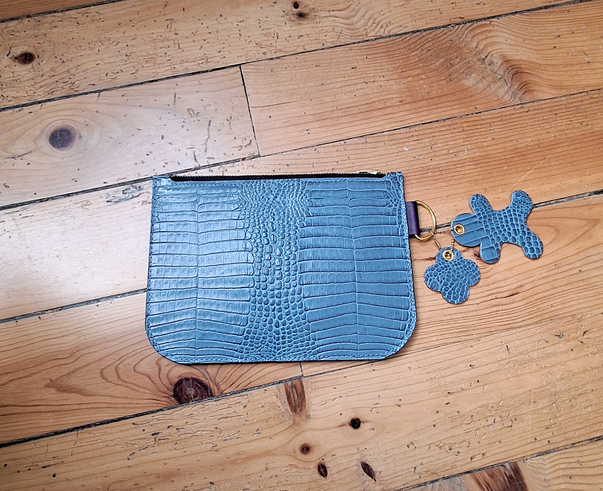 Pochette en cuir façon crocodile bleu ciel fermée par un zip doré. 