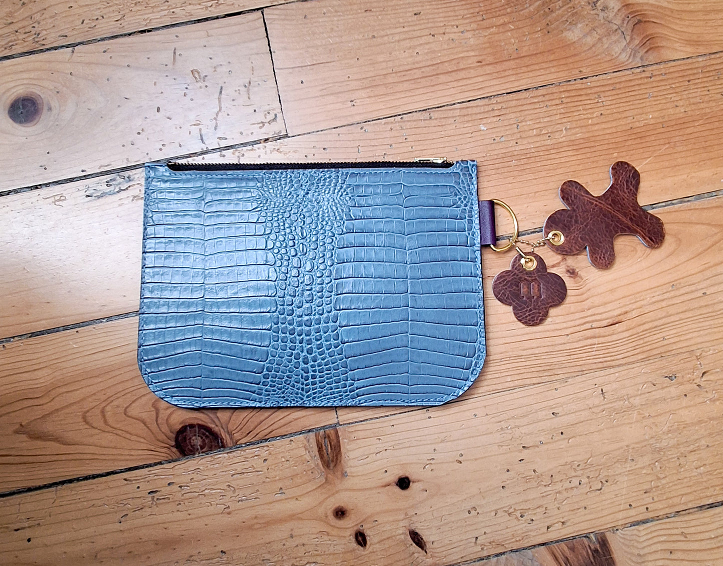 Pochette en cuir façon crocodile bleu ciel fermée par un zip doré. 