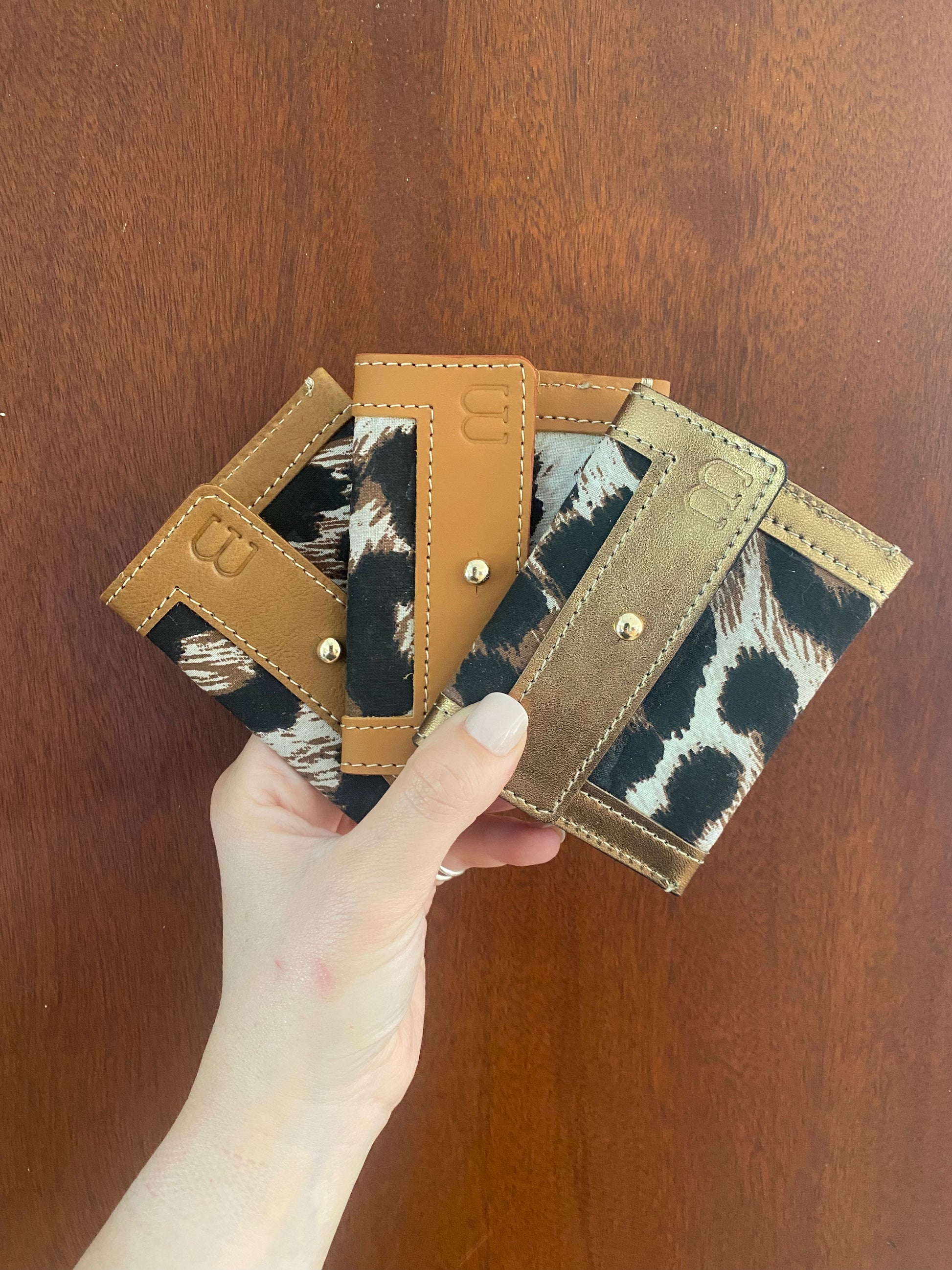 3 portes cartes en cuir camel et tissus léopard tenus dans une main 