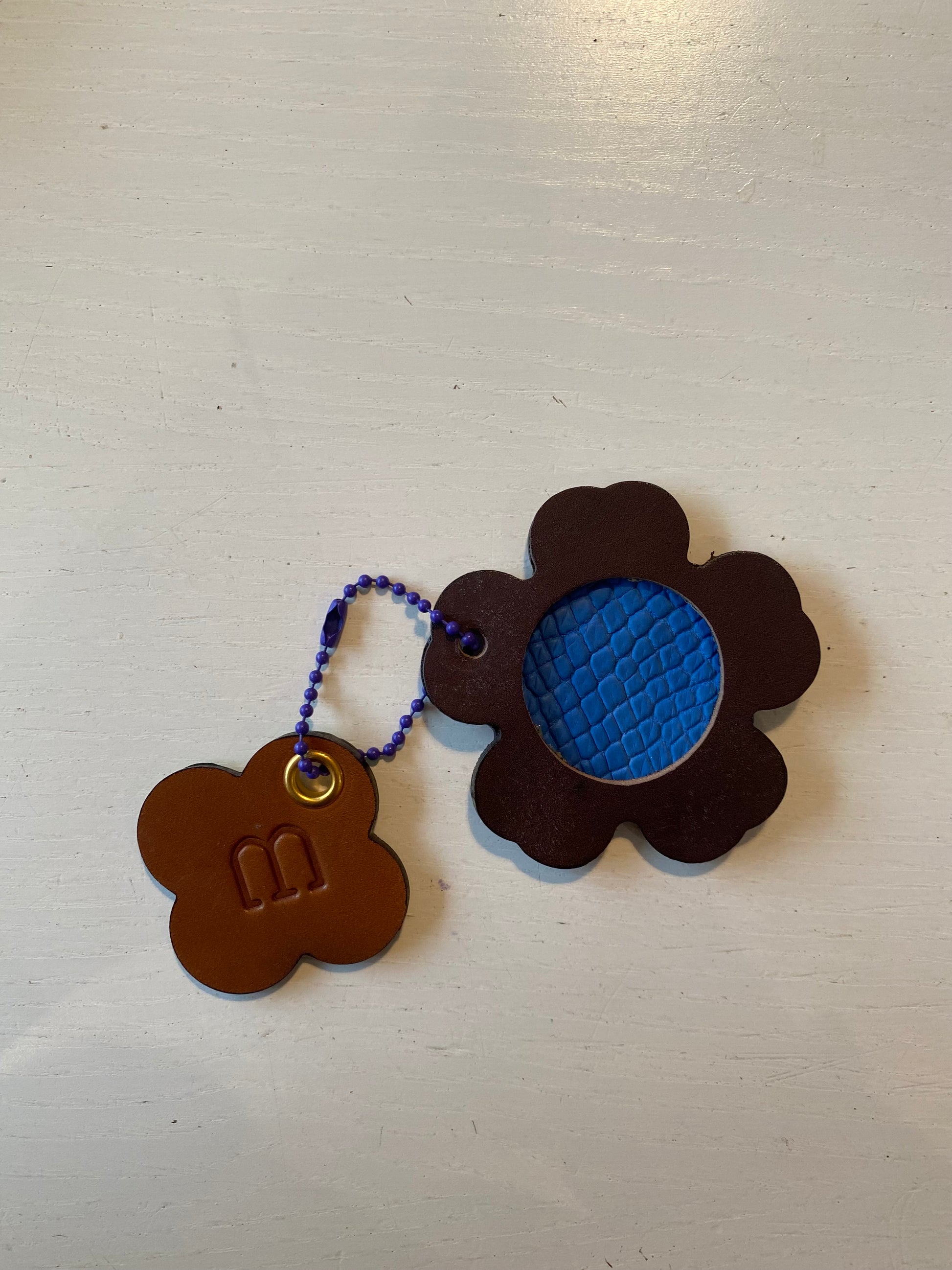 Porte clef en cuir composé de 2 éléments en forme de fleur et de trèfle sur fond blanc 