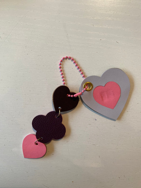 Porte clef en cuir composé de deux éléments dont un en forme de cœur et le second composé d’une suite de 3 petites formes florales et cœur 