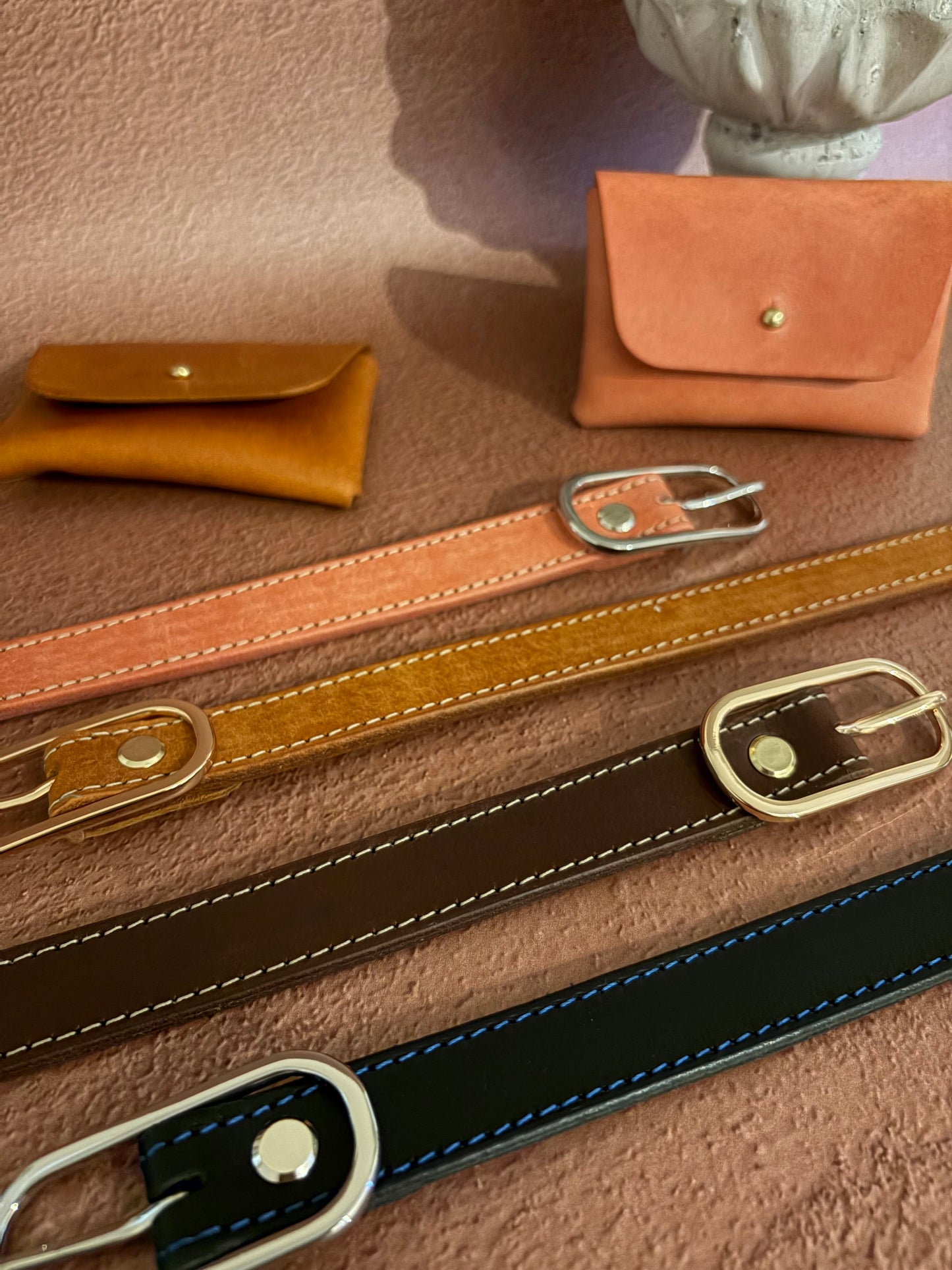 4 ceintures en cuir au tannage naturel sont posées sur un fond terracotta