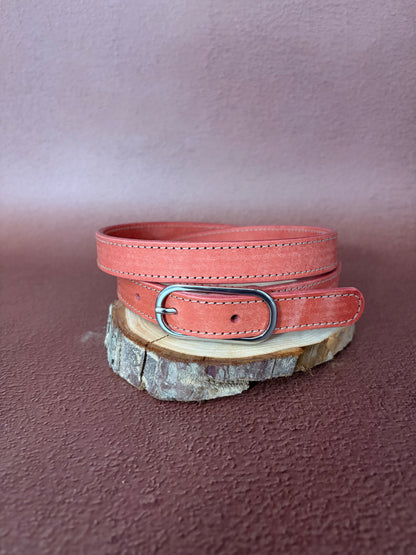 une ceinture en cuir tannage végétal rose avec une boucle ovale en acier est posée sur une tranche de bois le tout sur un fond ocre texturé