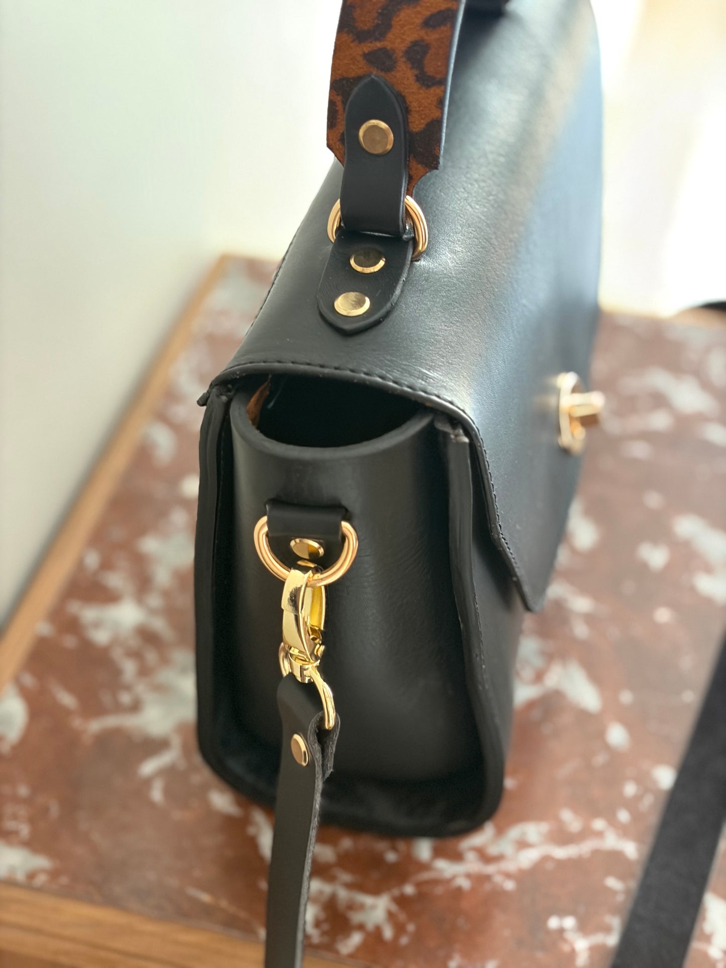 le sac est présenté de côté pour voir le détail de la bouclerie en laiton doré.