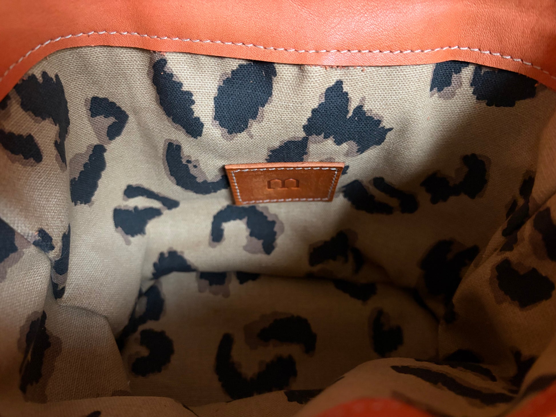 photo d'un détail de la doublure en coton du sac garance. un focus est fait sur l'étiquette en cuir sur laquelle est apposé le M de la marque. 