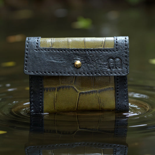 Porte cartes noir et vert kaki croco et sigle M embossé à droite comme en lévitation sur un lac se reflétant dans l'eau.