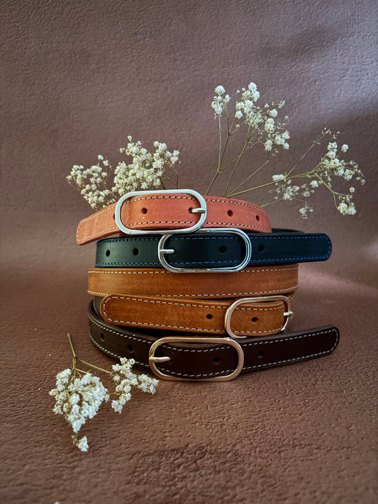 4 ceintures en cuir au tannage végétal sont empilées avec des fleurs blanches, le tout sur un fond ocre