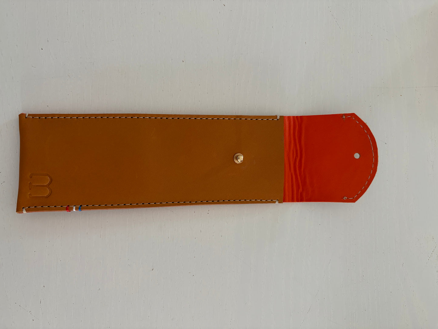 un étui en cuir marron doublé de cuir orange est présenté ouvert. 