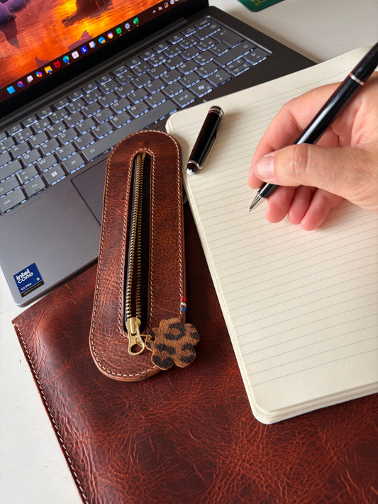 mise en scène d'un étui à crayon en cuir au tannage végétal wax avec un cahier un beau crayon et un ordinateur portable ouvert en fond.
