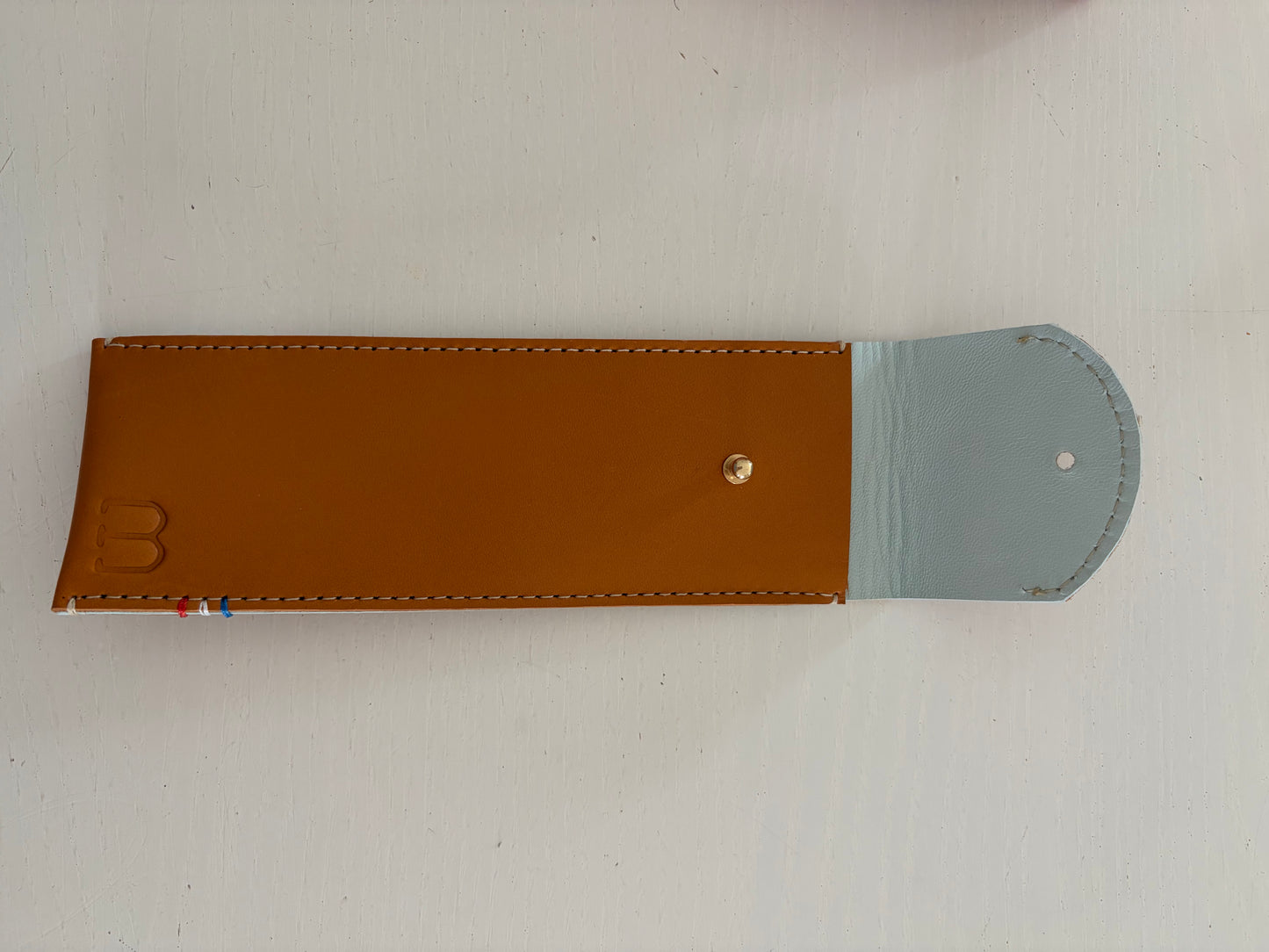 un étui en cuir marron doublé de cuir bleu ciel est présenté ouvert. 