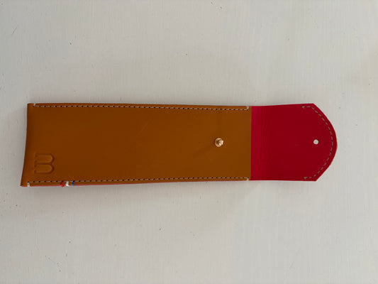 un étui en cuir marron doublé de cuir rouge framboise est présenté ouvert. 