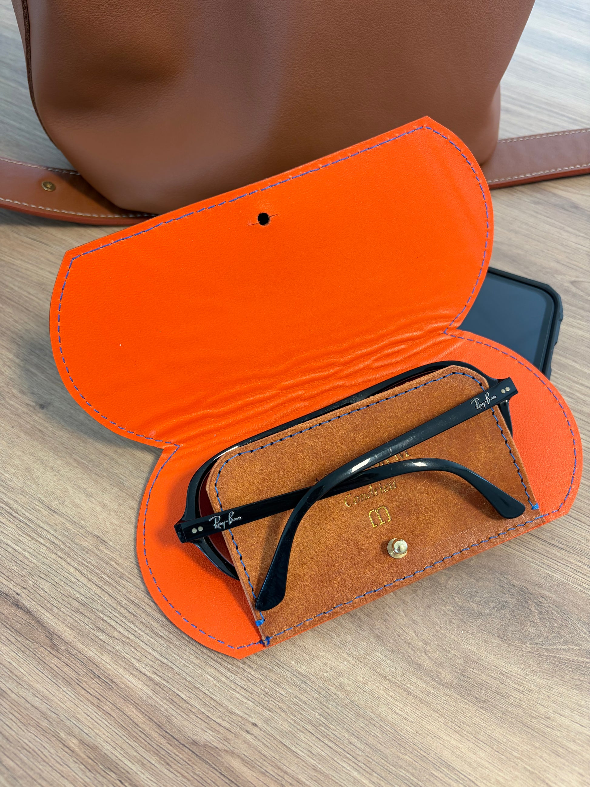 étui à lunettes en cuir au tannage végétal plat ouvert avec une paire de lunette dedans. Le tout sur une table en bois