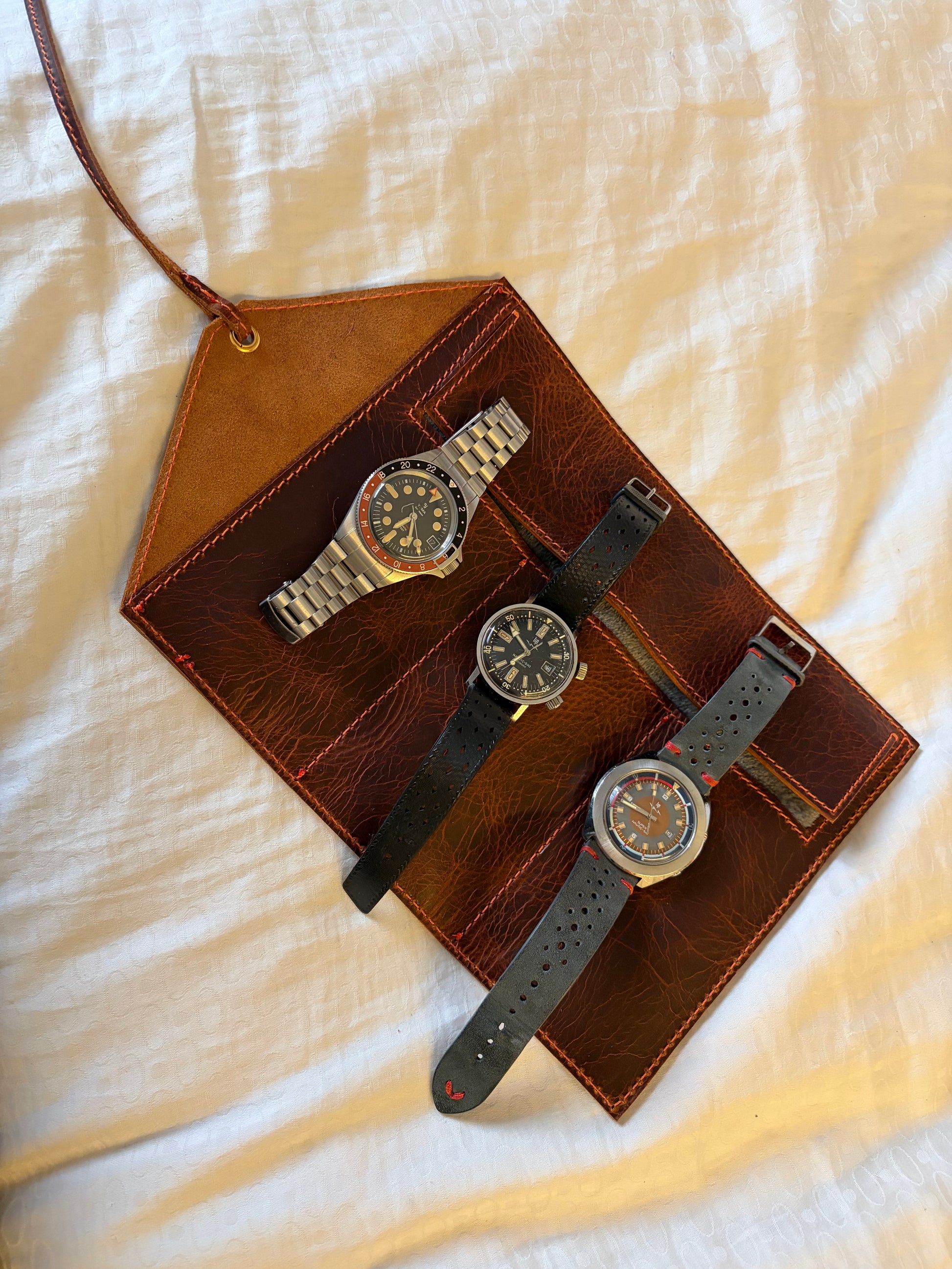 étui pour 3 montres en cuir wax ouvert et posé sur un drap blanc avec les 3 montres posé dessus. La vue est du dessus