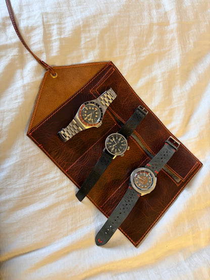 étui pour 3 montres en cuir wax ouvert et posé sur un drap blanc avec les 3 montres posé dessus. La vue est du dessus