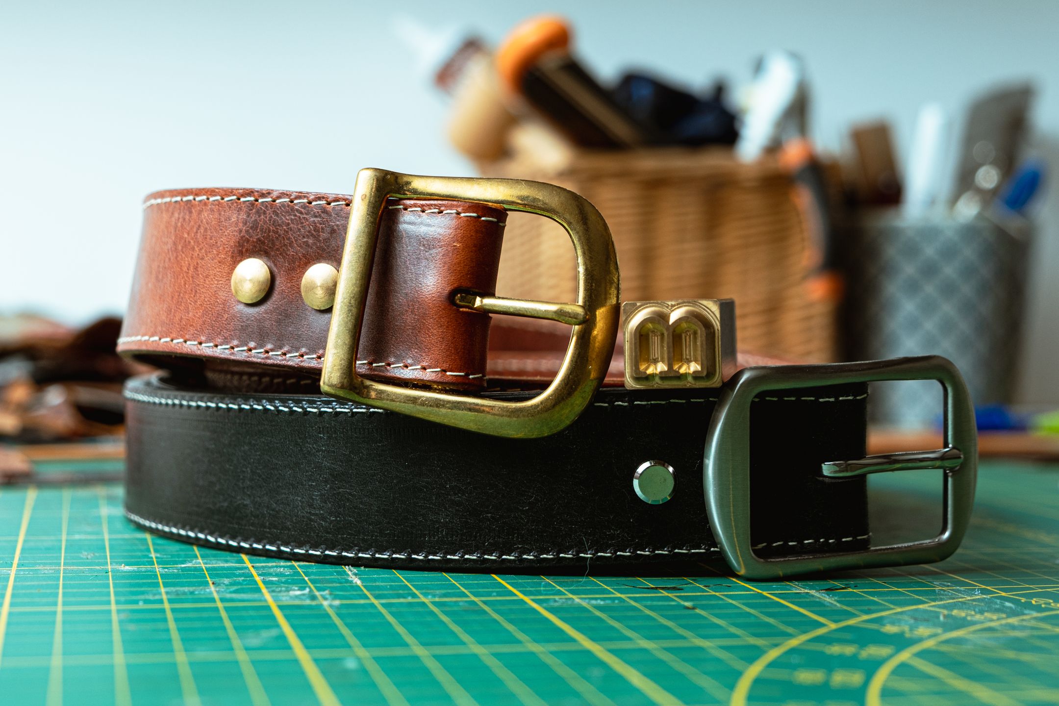 deux ceintures en cuir marron et noire l'une sur l'autre dans un atelier