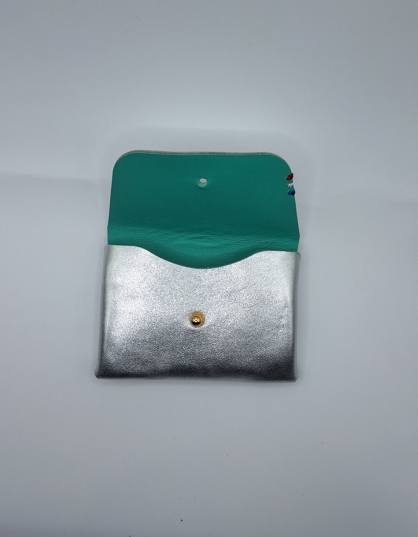 le porte carte est argenté et bleu vert. il est posé sur un fond blanc