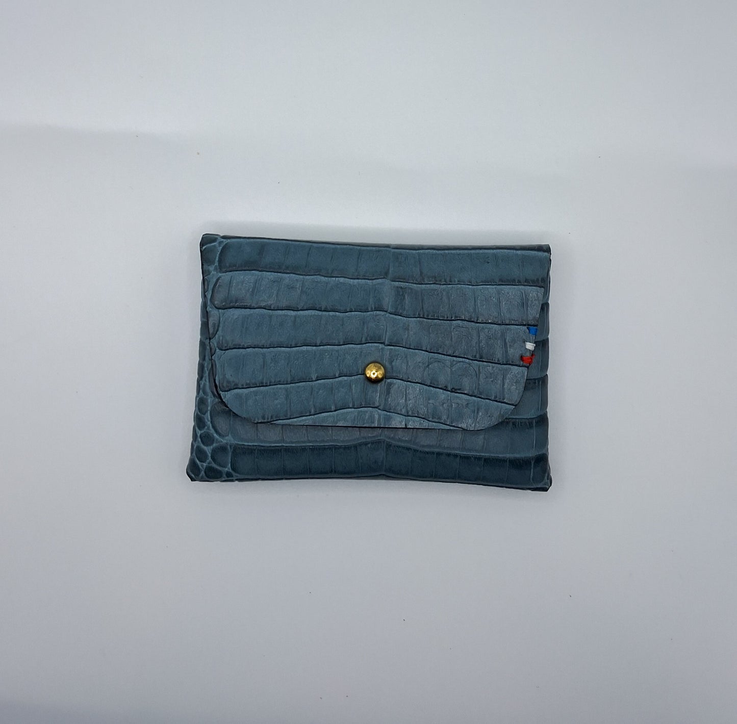 le porte carte est présenté fermé à plat sur un fond blanc. il est en cuir façon crocodile bleu.