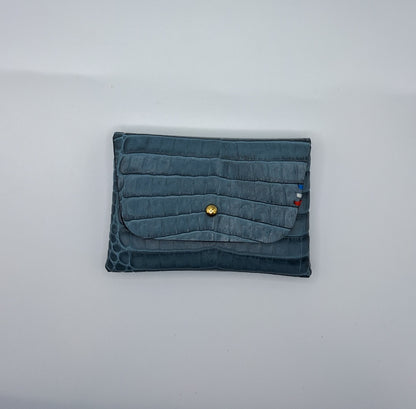 le porte carte est présenté fermé à plat sur un fond blanc. il est en cuir façon crocodile bleu.