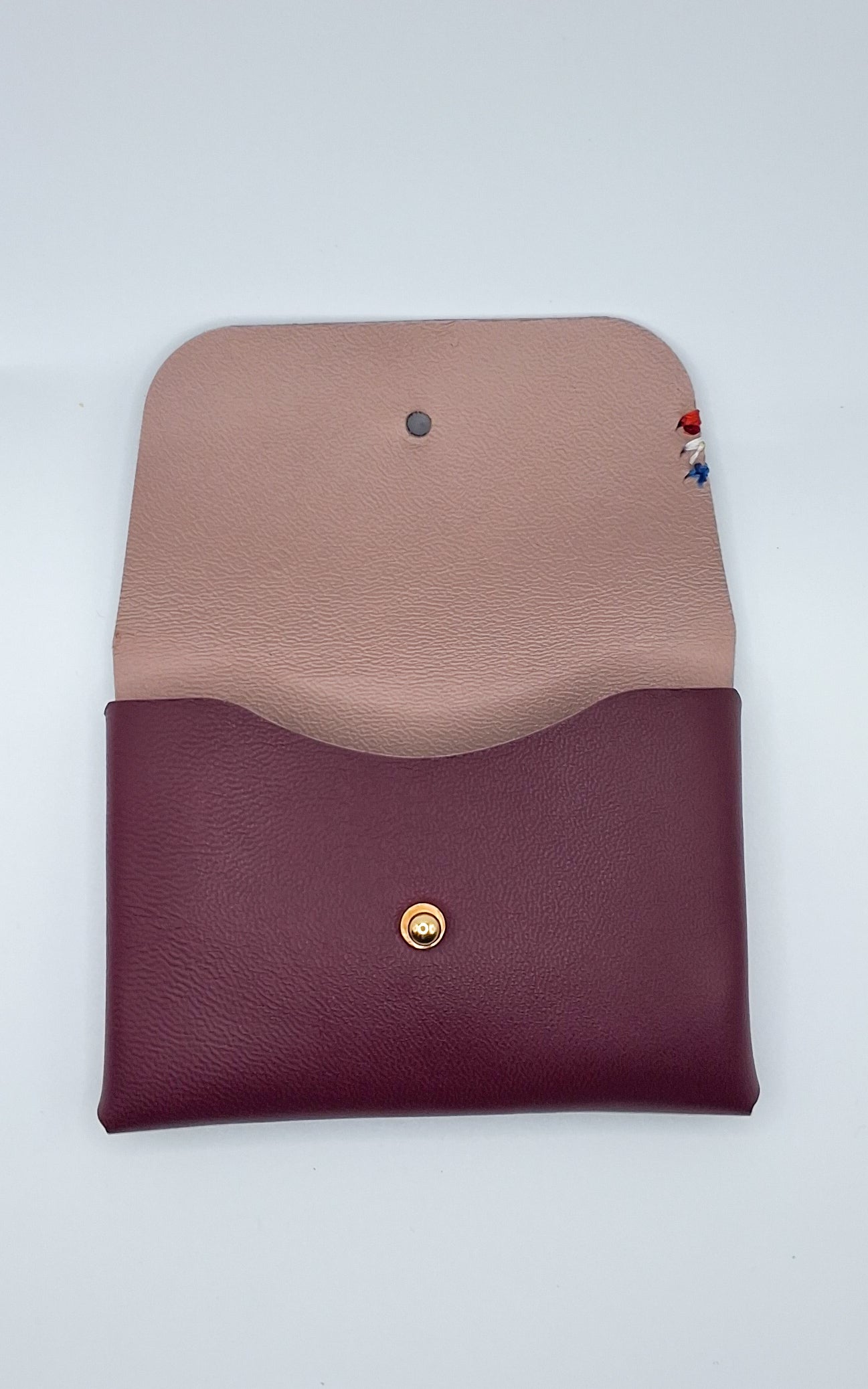 le porte carte est présenté ouvert à plat sur un fond blanc. il est de couleur rose foncé à l'extérieur et rose poudré à l'intérieur