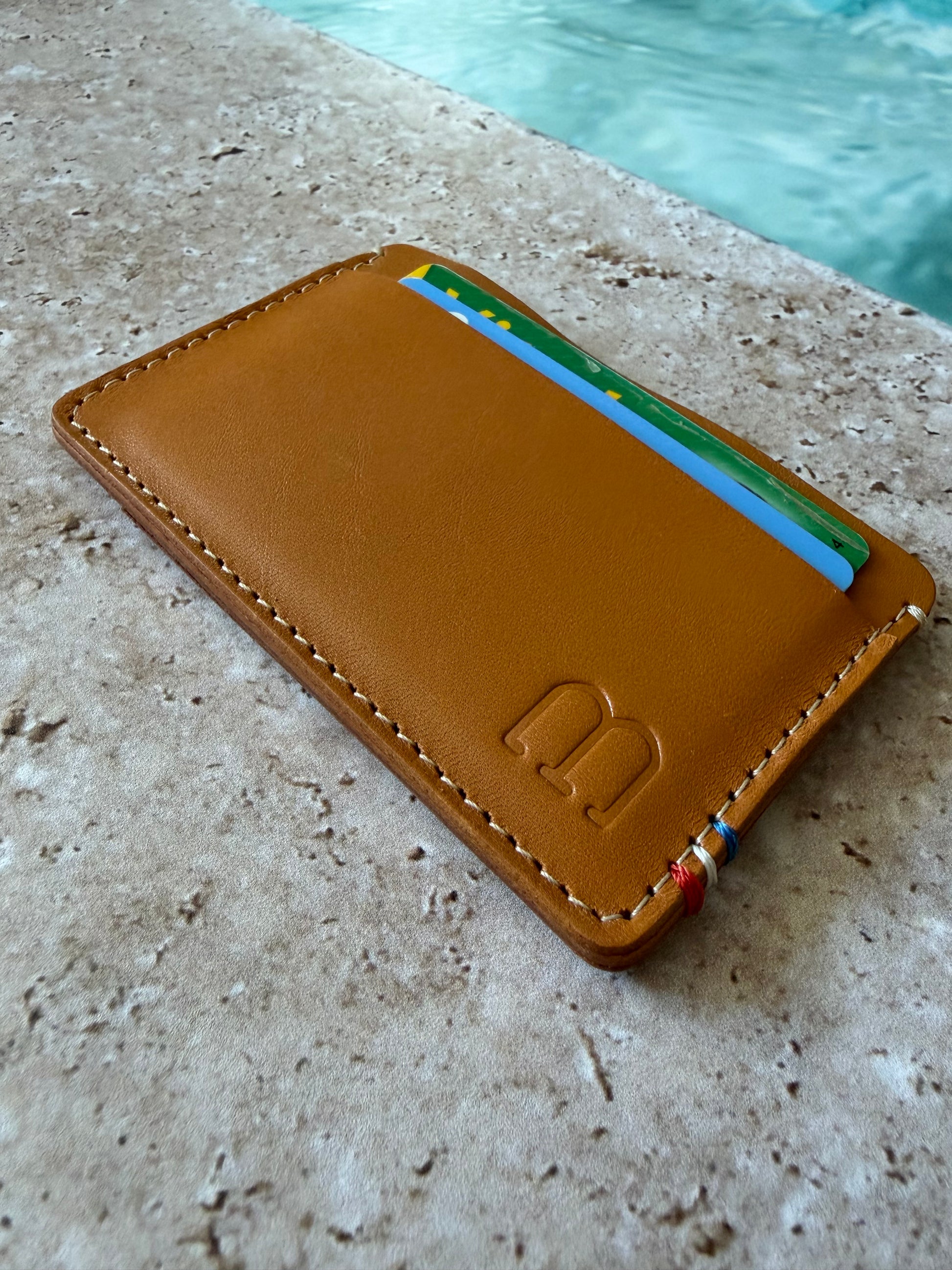 le porte carte est posé sur de la pierre au bord d'une piscine. il est vu en perspective avec le marquage M et la cocarde en premier plan. 