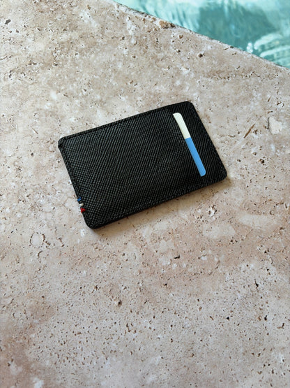 le porte carte en cuir noir saffiano est présenté à plat de dos sur une pierre de bord de piscine. 