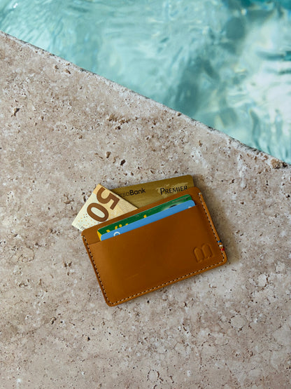 le porte carte est posé sur une pierre au bord d'une piscine. les poches du porte carte sont garnies de cartes et de billet
