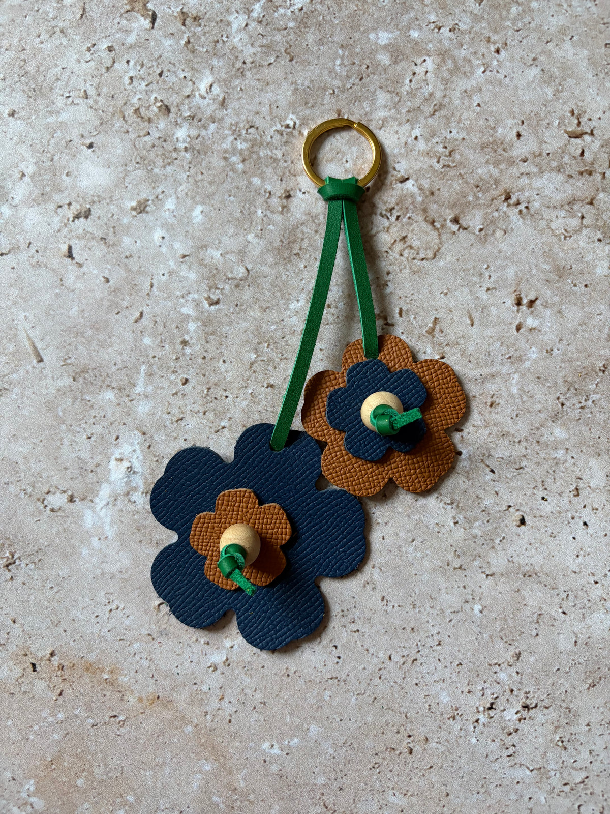 le porte clefs en cuir en forme de fleures bleues et marrons est présenté à plat sur un fon den travertin. 