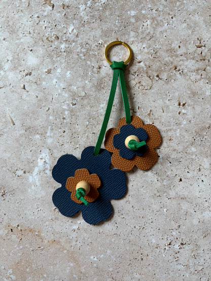 le porte clefs en cuir en forme de fleures bleues et marrons est présenté à plat sur un fon den travertin. 