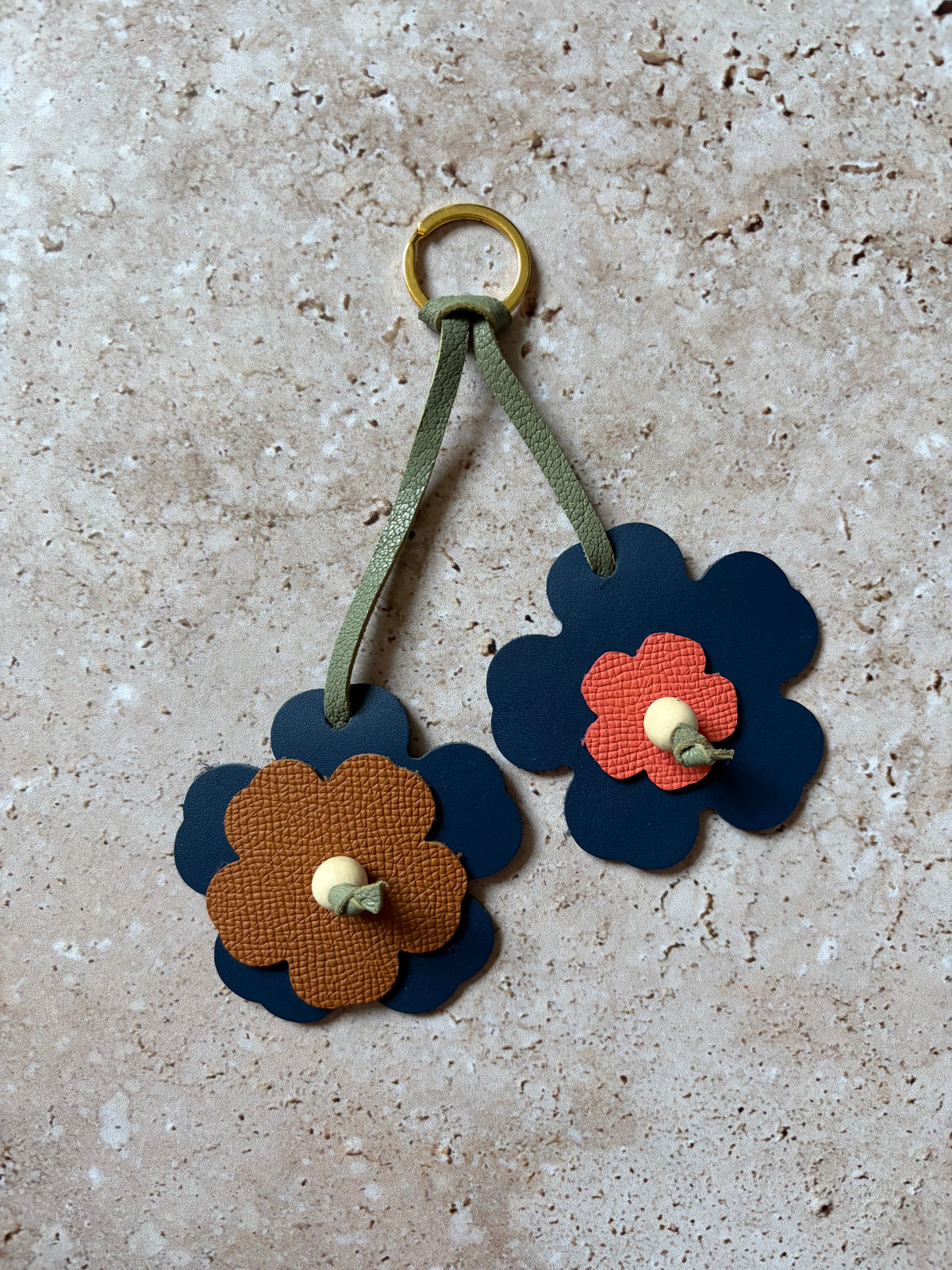 le porte clefs en cuir en forme de fleurs bleu, corail et marrons est présenté à plat sur un fon den travertin. 