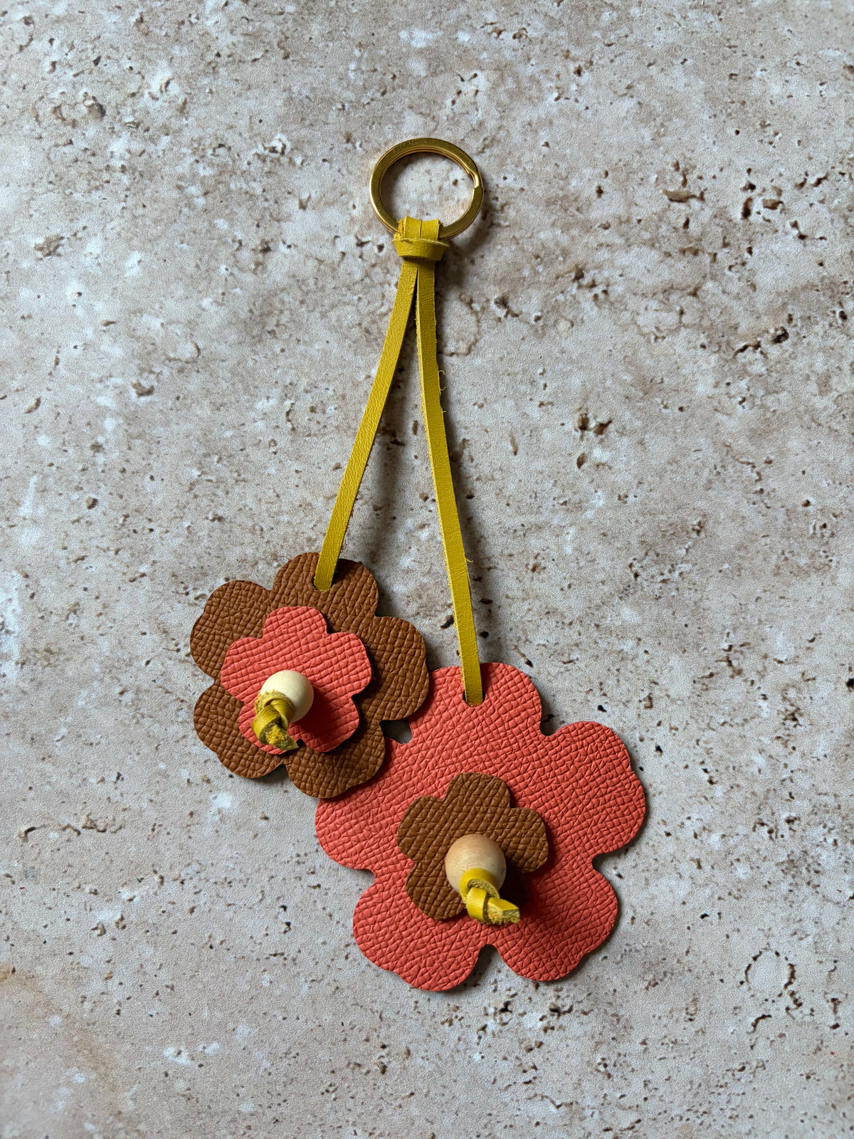 le porte clefs en cuir en forme de fleures corail et marron est présenté à plat sur un fon den travertin. 