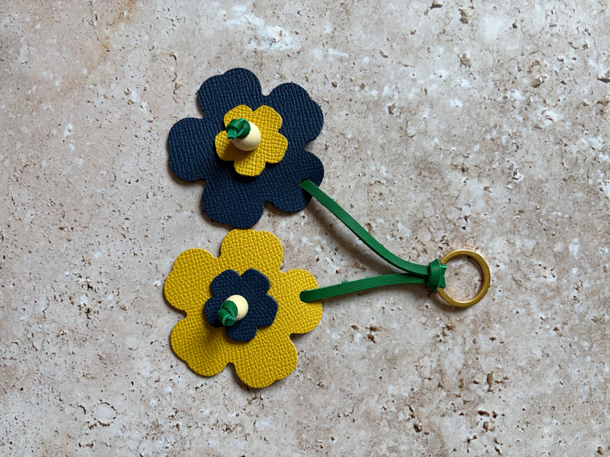 le porte clefs en cuir en forme de fleures bleu et jaune est présenté à plat sur un fon den travertin. 